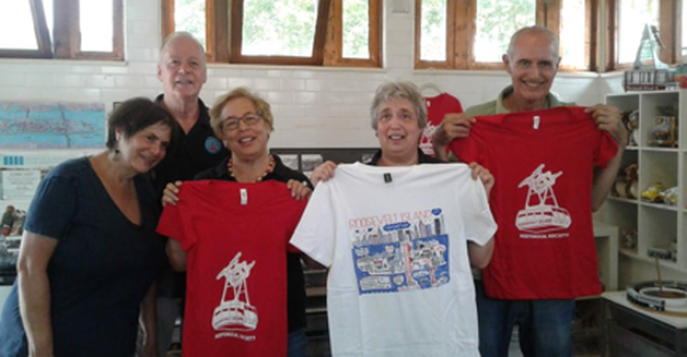 Five RIHS volunteers holding up Roosevelt Island T-shirts inside the kiosk.