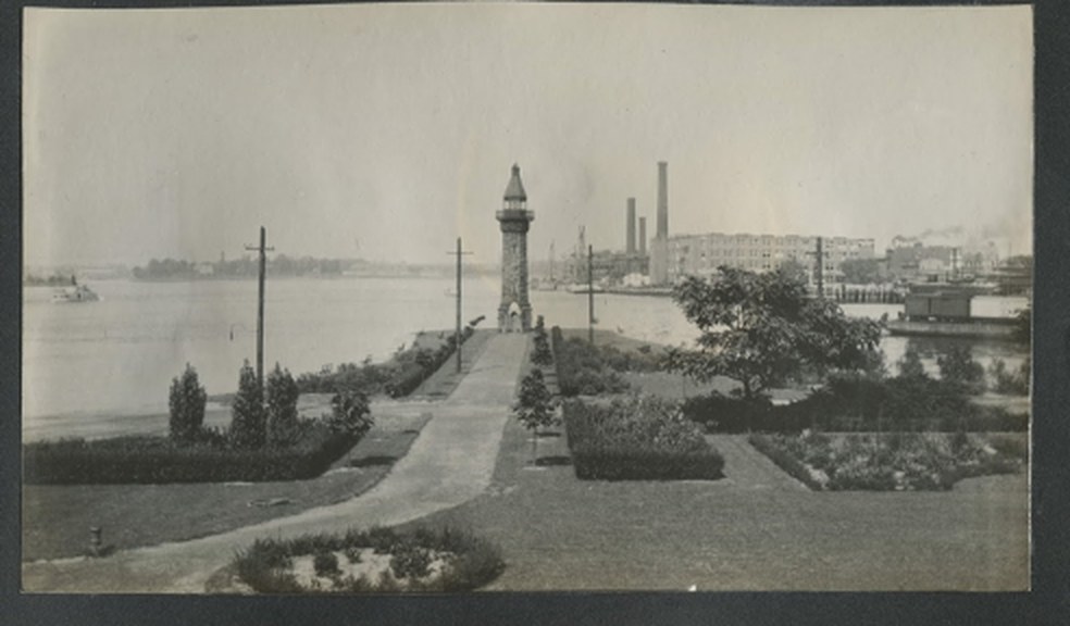 Historic photograph of the Blackwell Island Lighthouse at the island's north tip, with formal gardens in the foreground and the Manhattan shoreline beyond.